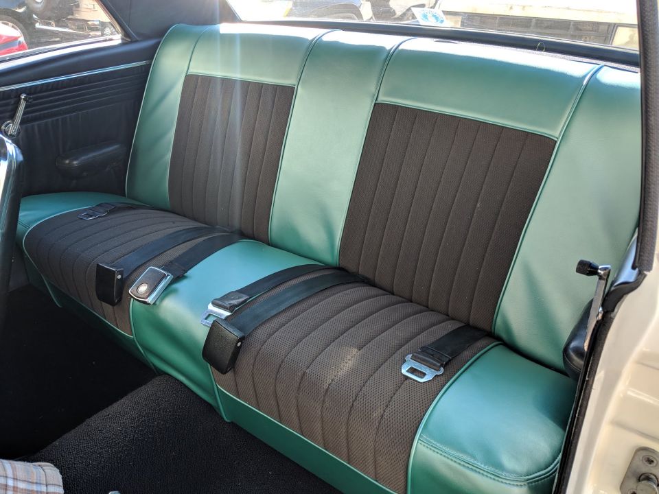 Teal green and gray vinyl rear bench seat with lap belts in a classic car interior