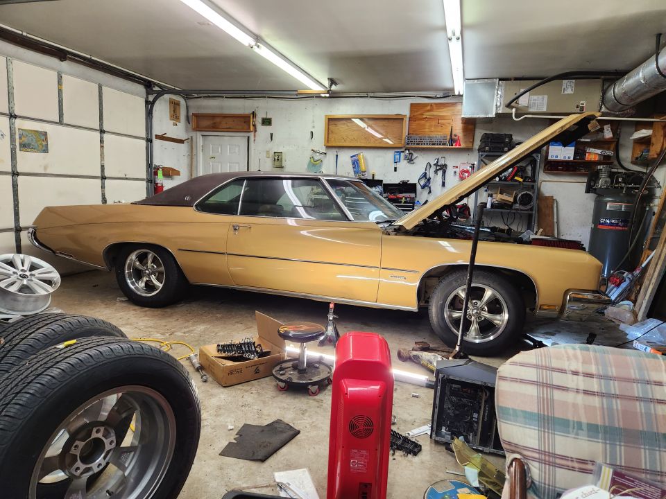 Gold 1970s coupe with brown vinyl roof and hood open in garage.