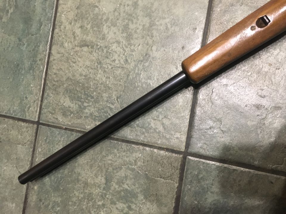 Close-up of a rifle barrel and wooden stock resting on a tiled floor
