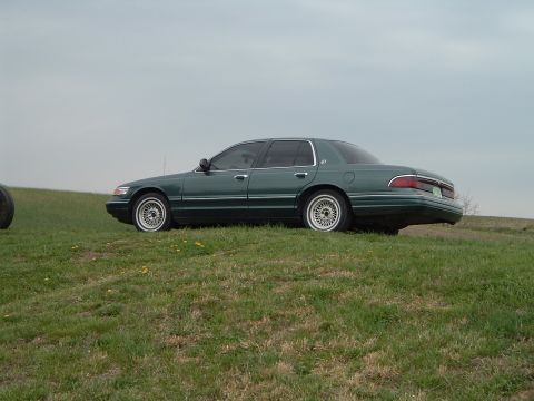 1995 Mercury Grand Marquis - A 1995 Mercury Grand Marquis is seen from the side, parked on a grassy incline under an overcast sky.