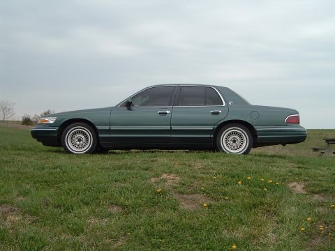 1995 Mercury Grand Marquis - Side profile of a 1995 Mercury Grand Marquis sedan on a grassy knoll under an overcast sky.