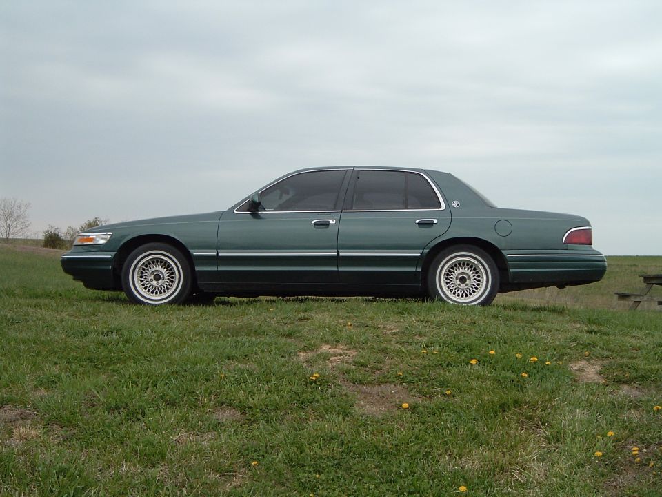 Green Mercury Grand Marquis sedan side profile on grass with lace-spoke alloy wheels