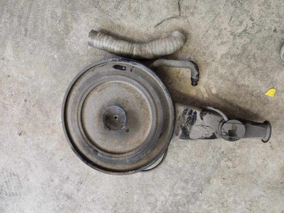Round air cleaner assembly with metal hose and plastic intake tube on concrete.