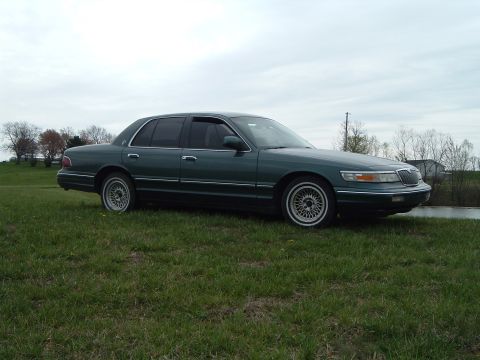 1995 Mercury Grand Marquis - A 1995 Mercury Grand Marquis is shown from a 3/4 front angle, parked on a grassy area with a cloudy sky above.