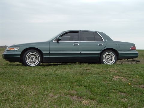 1995 Mercury Grand Marquis - A 1995 Mercury Grand Marquis sedan is shown from the side, parked on a grassy area under an overcast sky.