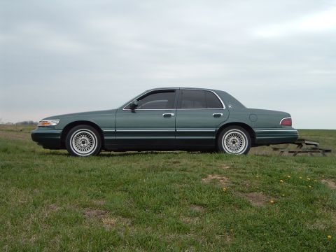 1995 Mercury Grand Marquis - This 1995 Mercury Grand Marquis is seen from the side, parked on a grassy incline under an overcast sky.