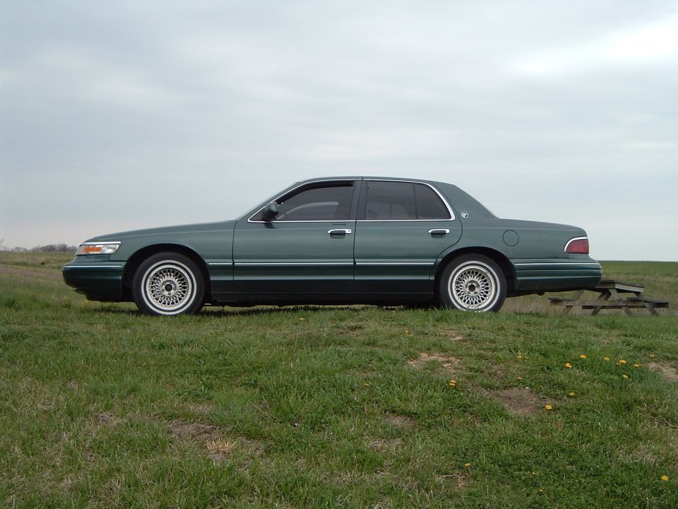 Green 1995 Mercury Grand Marquis sedan, side view, parked on a grassy hill