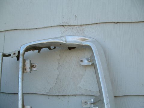 1979 Ford Bronco - A damaged chrome grille surround is shown against a weathered clapboard wall.
