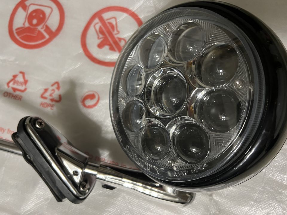 Round black LED headlight with chrome mount on white surface with symbols