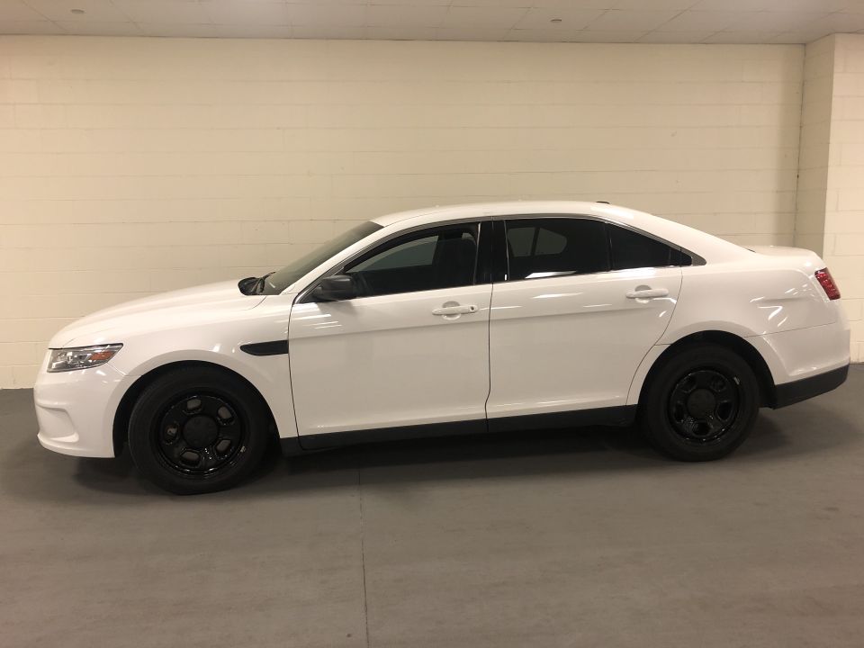 White 2013 Ford Taurus sedan parked indoors, side view.