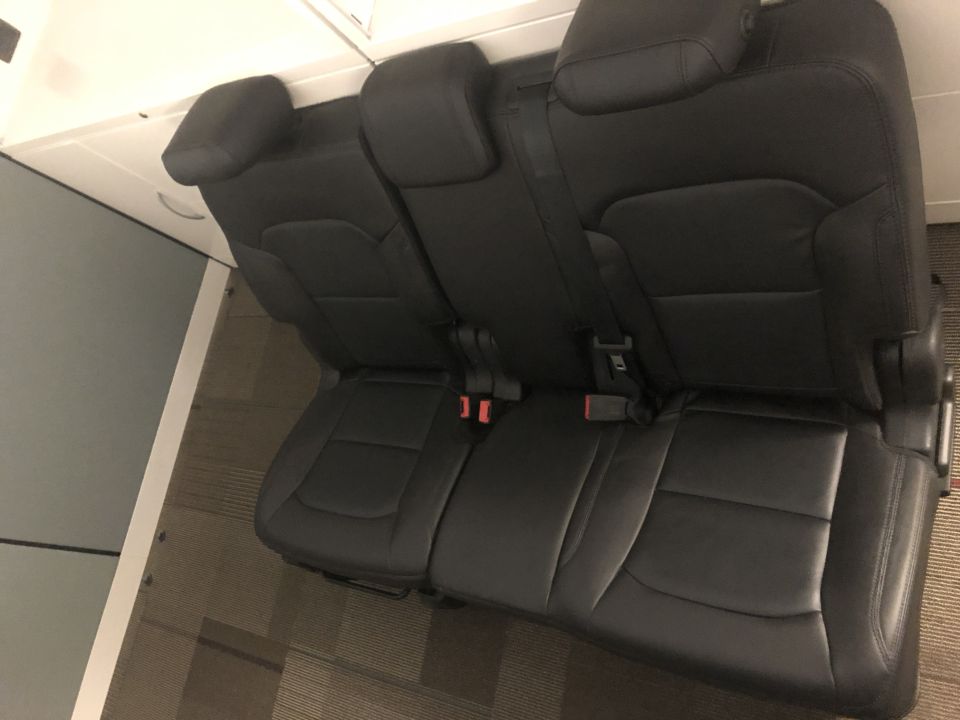 Removed black leather rear bench seat with headrests and seat belts on office carpet
