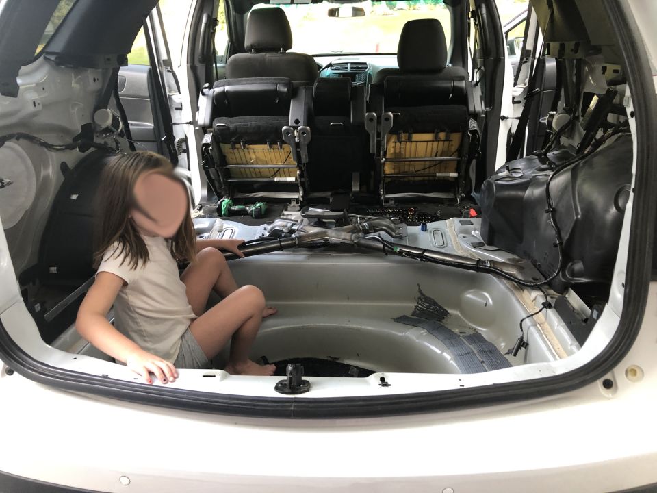 Child sitting in the stripped-out interior of an SUV, showing exposed metal and wiring