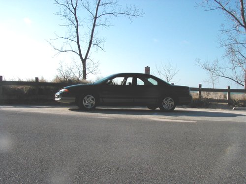 Side profile of dark teal Dodge Intrepid sedan parked by a rail fence