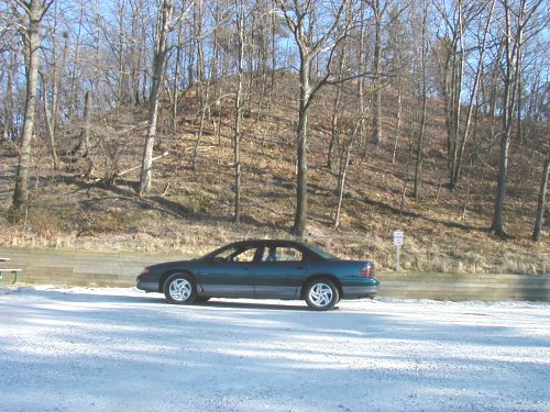 dark green sedan parked near trees and a hill