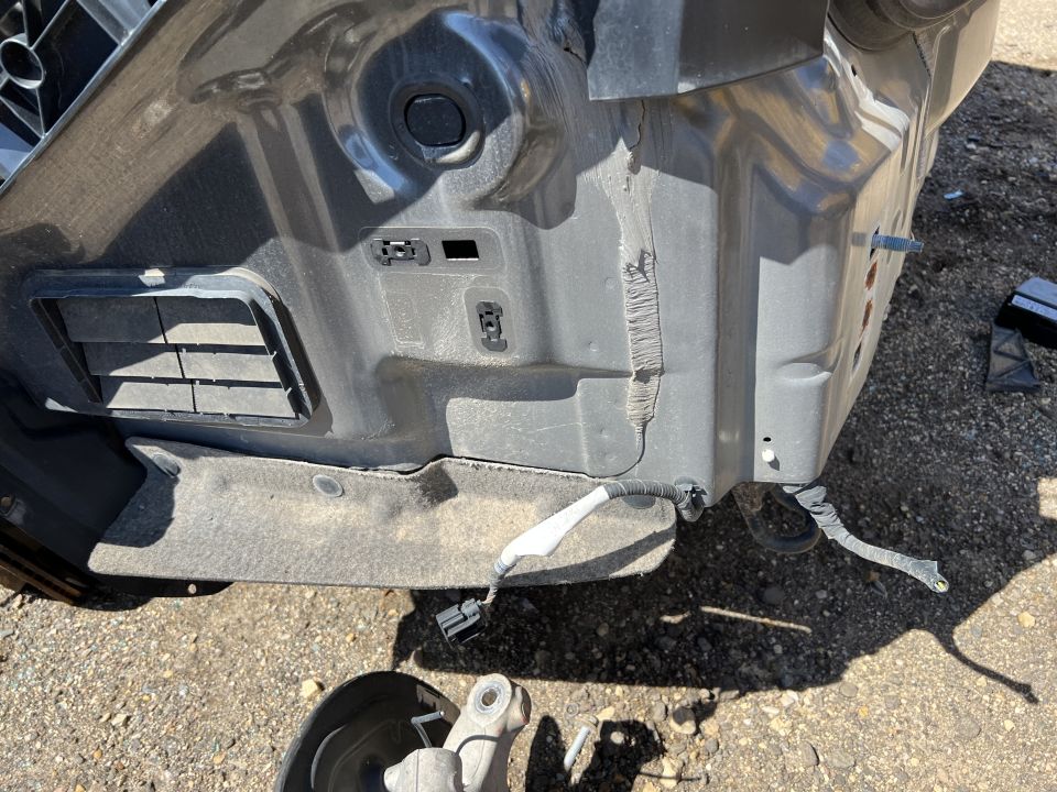 Underside of a vehicle's front bumper area, showing a black grille and wiring.