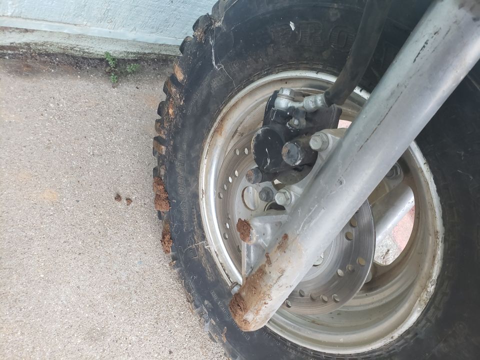 Motorcycle front wheel, tire, suspension, brake rotor and caliper with mud.