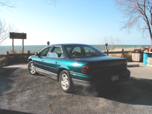1995 Dodge Intrepid parked near a beach with a wooden fence and a sign