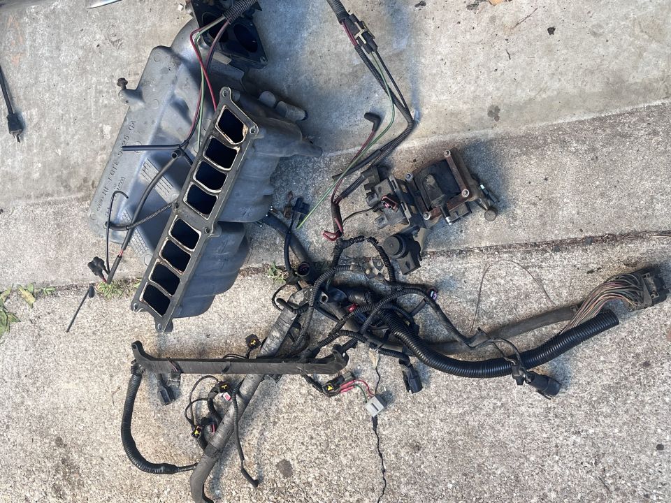 Removed intake manifold and engine wiring harness laid out on concrete pavement