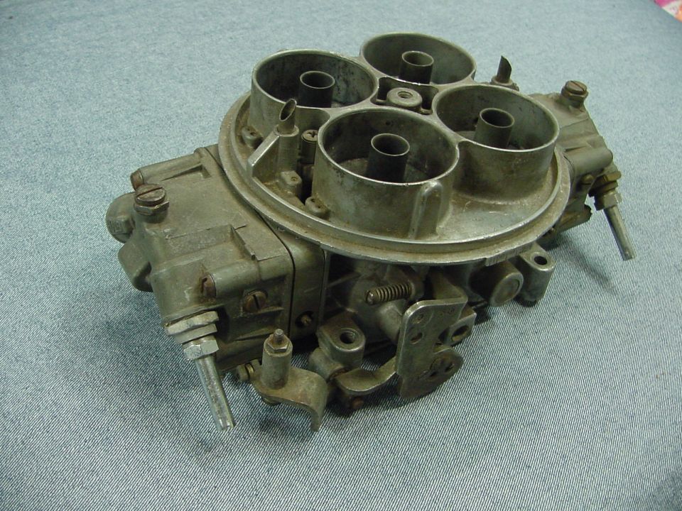 Four-barrel carburetor on a blue textured surface.