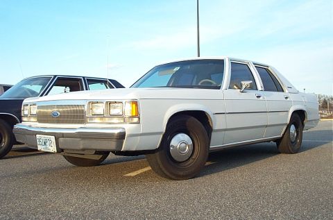 1991 Ford LTD Crown Victoria - White 1980s Ford sedan with a chrome grille and hubcaps, parked outdoors.