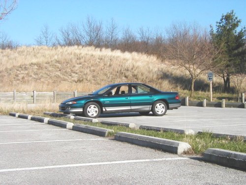 Green sedan parked in a lot with a grassy hill behind it
