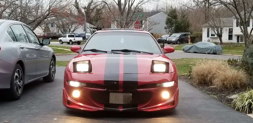 Front view of red sports car with black and red racing stripes and projector headlights in driveway
