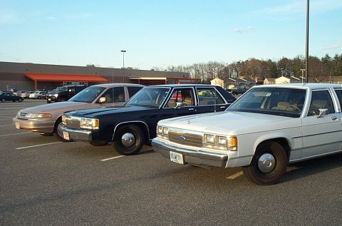 1991 Ford LTD Crown Victoria - Three Ford Crown Victorias are parked in a lot. The front car is white, the middle is black, and the rear is tan.