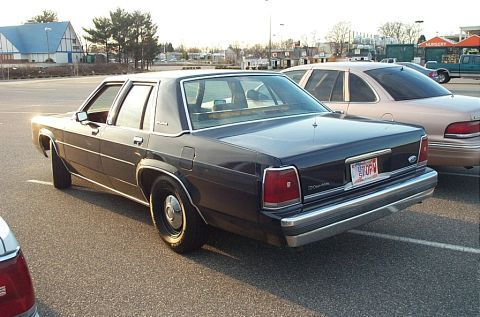 1991 Ford LTD Crown Victoria - A dark blue sedan is parked in a lot, showing its rear and side profile with a visible license plate.