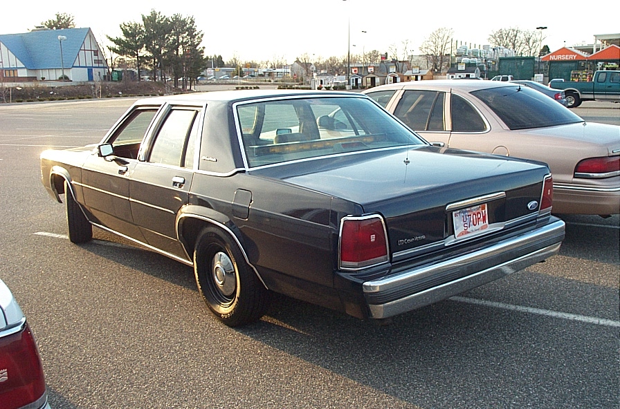Dark blue sedan parked in a lot, rear view. License plate reads '97 TOPW'