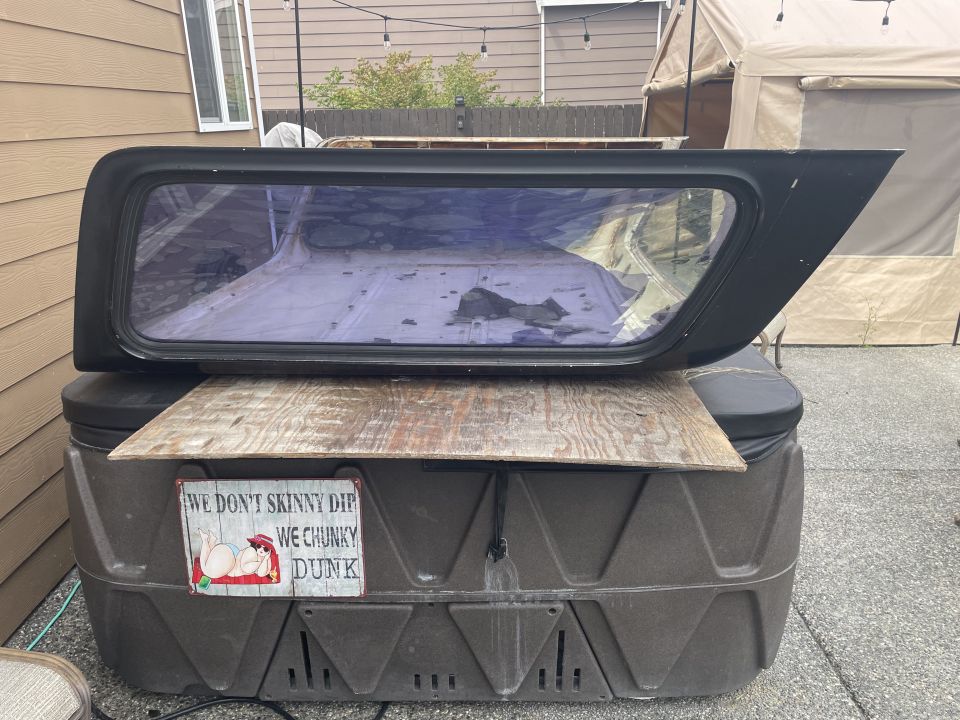 Black truck cap with tinted window on top of a hot tub with a funny sign.
