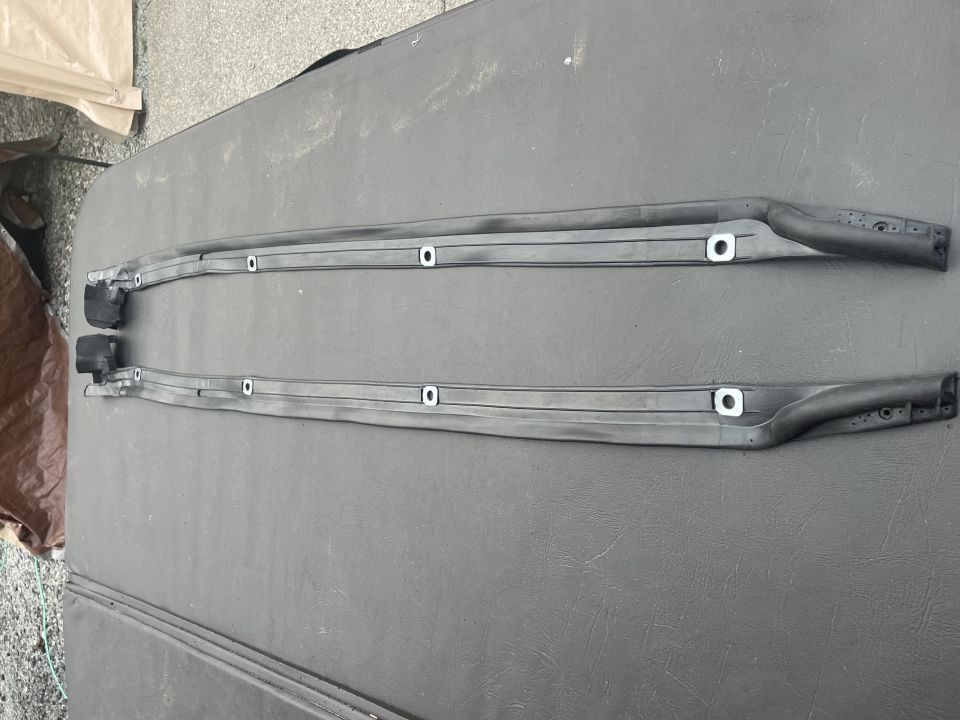 Two black roof rack rails with mounting holes and rubber end caps.