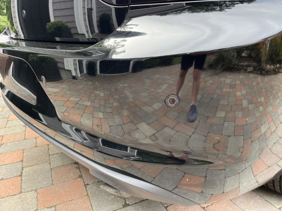 Close-up of a black car front bumper reflecting pavers and surroundings