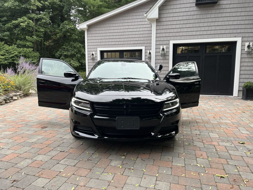 Black Dodge Charger with both front doors open, front view on driveway