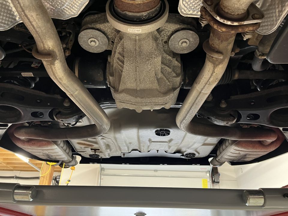 Underbody view of a car showing rear differential and exhaust pipes on a lift
