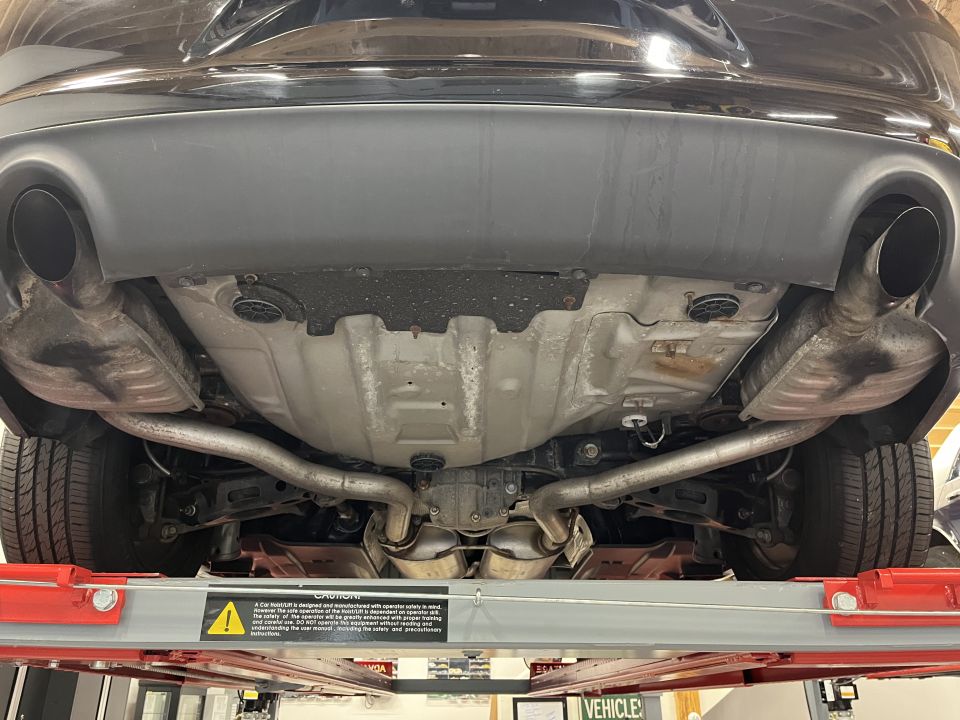 Rear underbody view of a car on a lift showing dual exhaust tips and fuel tank