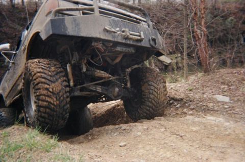 1992 Ford Bronco - This heavily modified off-road vehicle navigates a challenging dirt path with its large, mud-caked tires.