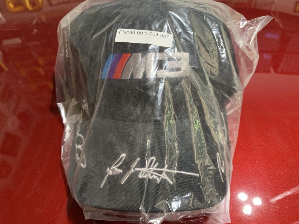 Black BMW M cap in plastic packaging with a white label.