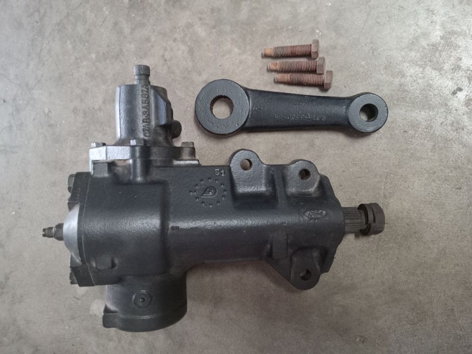 Black Ford steering gear box, pitman arm, and bolts on concrete.
