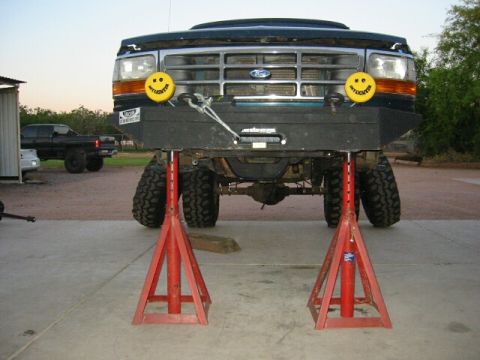 1994 Ford Bronco - This Ford truck is on jack stands, showing its front end with a winch and custom bumper with smiley face lights.