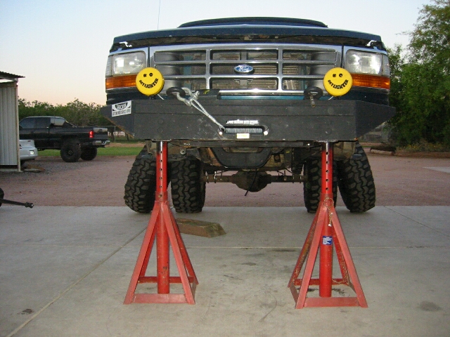Front of lifted dark Ford truck on red jack stands with smiley decals and big tires