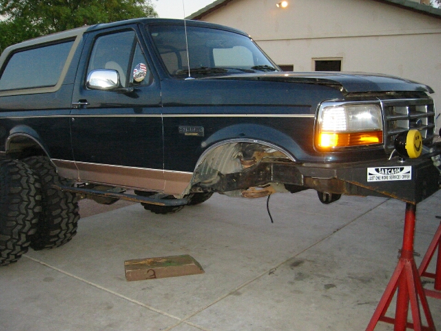 Dark green Ford Bronco on lift with front fender removed, large off-road tires