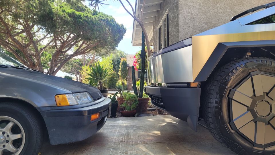 Tesla Cybertruck's unique wheel and fender next to a dark gray car.