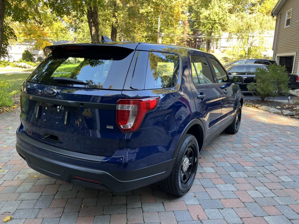 Rear three-quarter view of a dark blue Ford Explorer SUV on a brick driveway