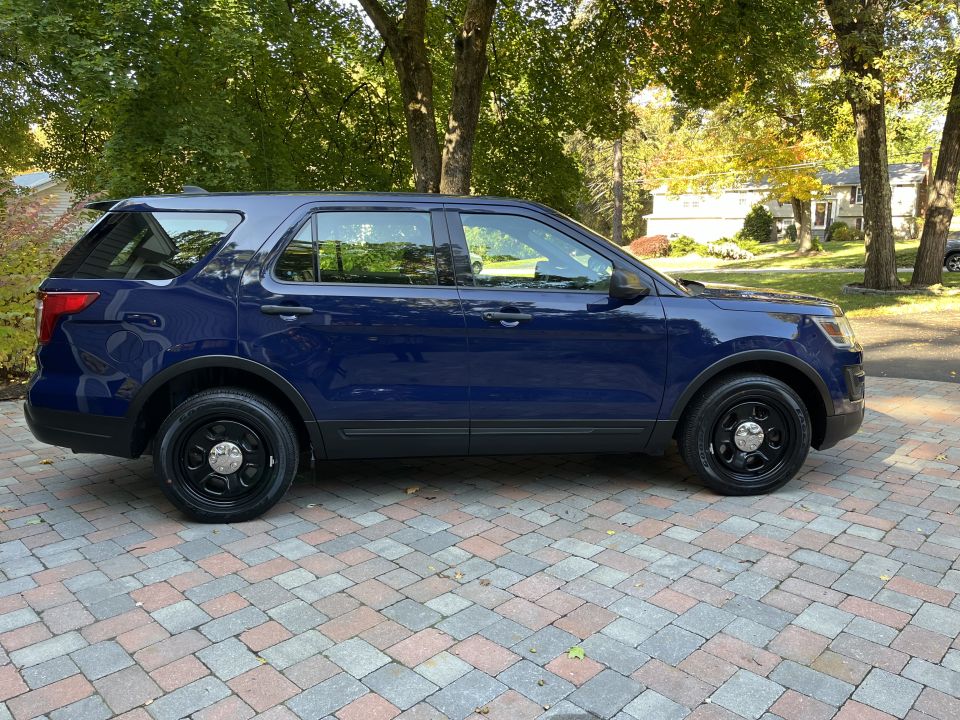 Passenger-side profile of a dark blue Ford Explorer SUV on a brick driveway