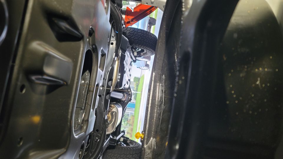 Underside view of a vehicle showing suspension, exhaust, and a yellow tow hook.