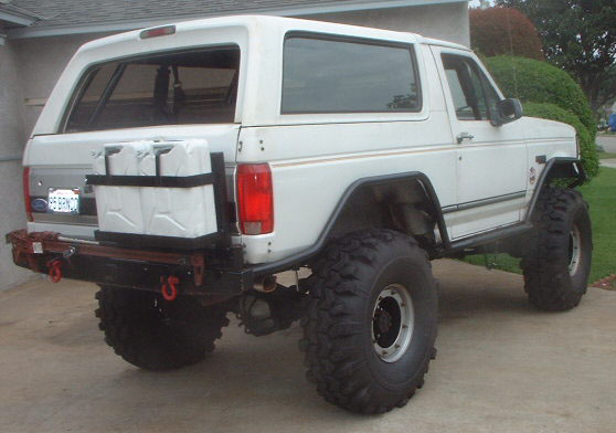 Rear of white lifted full-size Bronco on mud tires with tube bumper and jerry cans