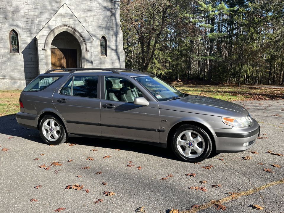 Gray Saab 9-5 wagon parked on asphalt with fallen leaves, side view
