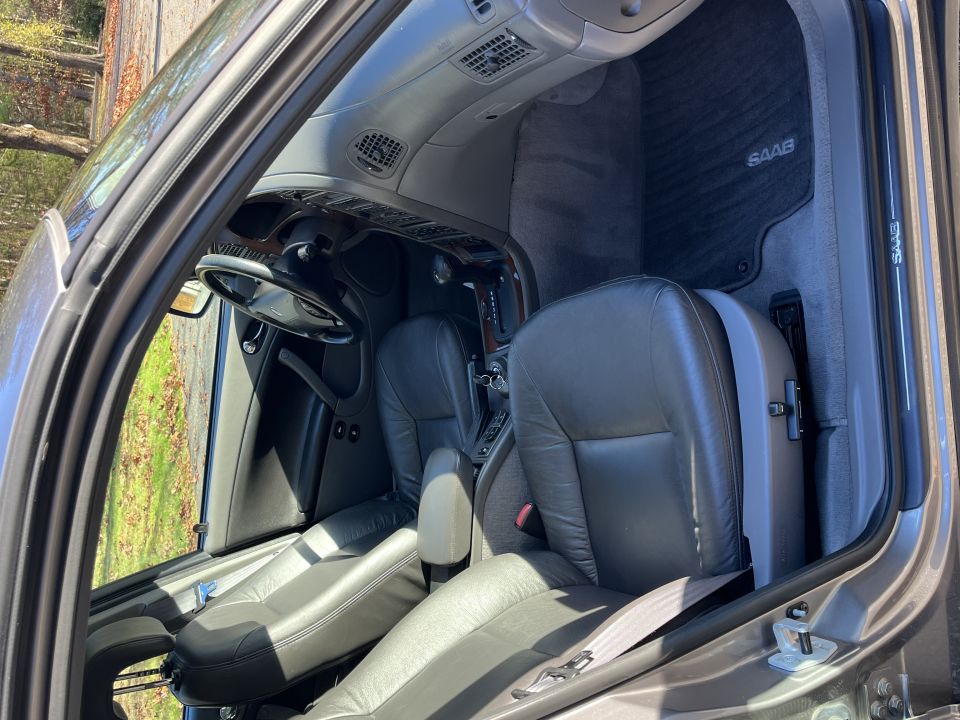 Gray leather seats and dashboard of a car with a SAAB floor mat visible