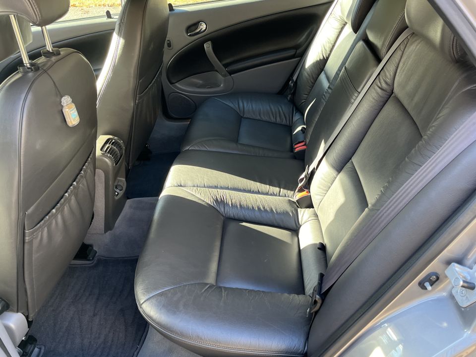 Car interior with black leather rear seats, gray carpet, and a small air freshener hanging from a headrest