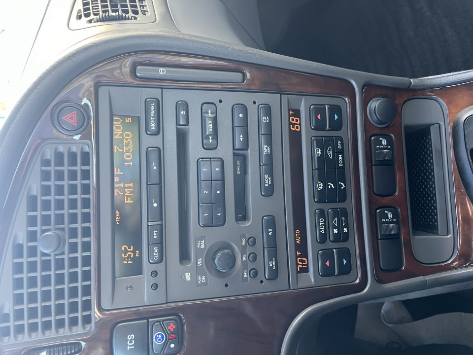 Car interior dashboard with wood trim, showing climate controls, radio, and a digital display with time and temperature